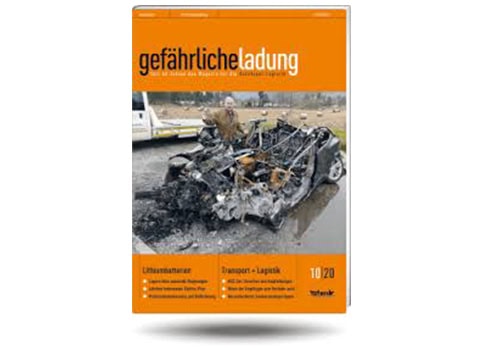 Titelblatt eines Magazins mit einem ausgebrannten Autowrack und einer lächelnden Person im Hintergrund.