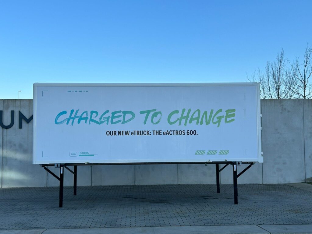 A large white container with green text ‘Charged to Change’ in front of a concrete wall.
