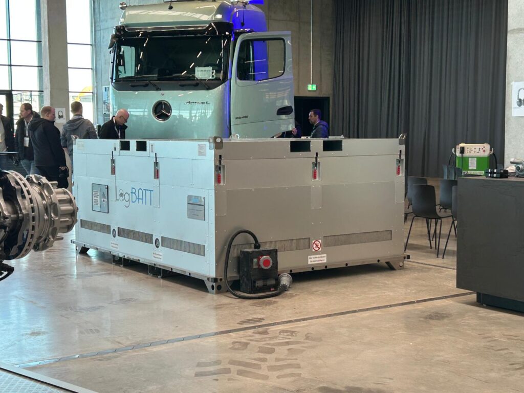 A silver lorry is parked behind a large logistics box in the indoor area.