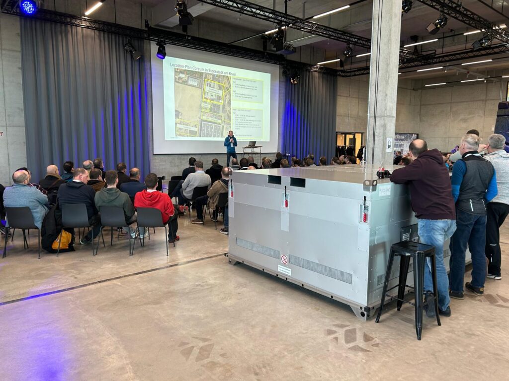 A group of people at a presentation in a hall, the room has a simple and modern design.