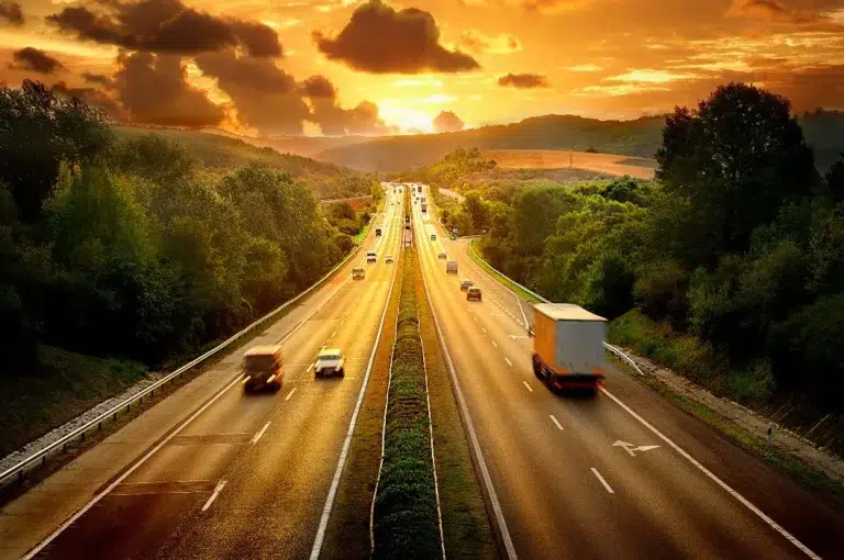 Autobahn im Sonnenuntergang mit leuchtendem Himmel und Bäumen am Rand.