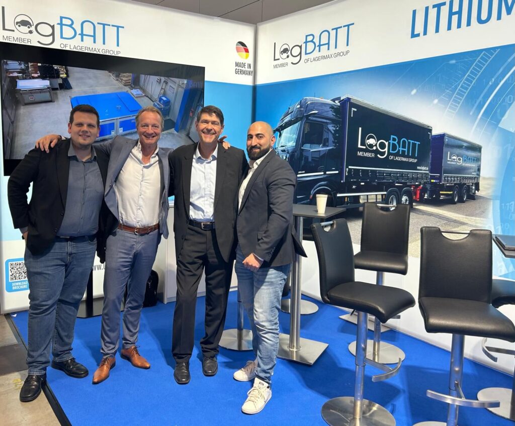 Drei Männer und eine Frau lächeln vor einem Logistik-Stand mit blauen Lithium-Akzenten.