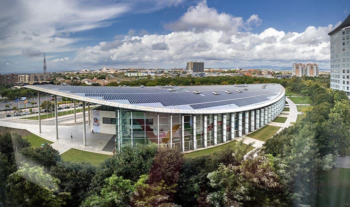 Moderne, gebogene Glasarchitektur, eingebettet in eine grüne Parklandschaft.