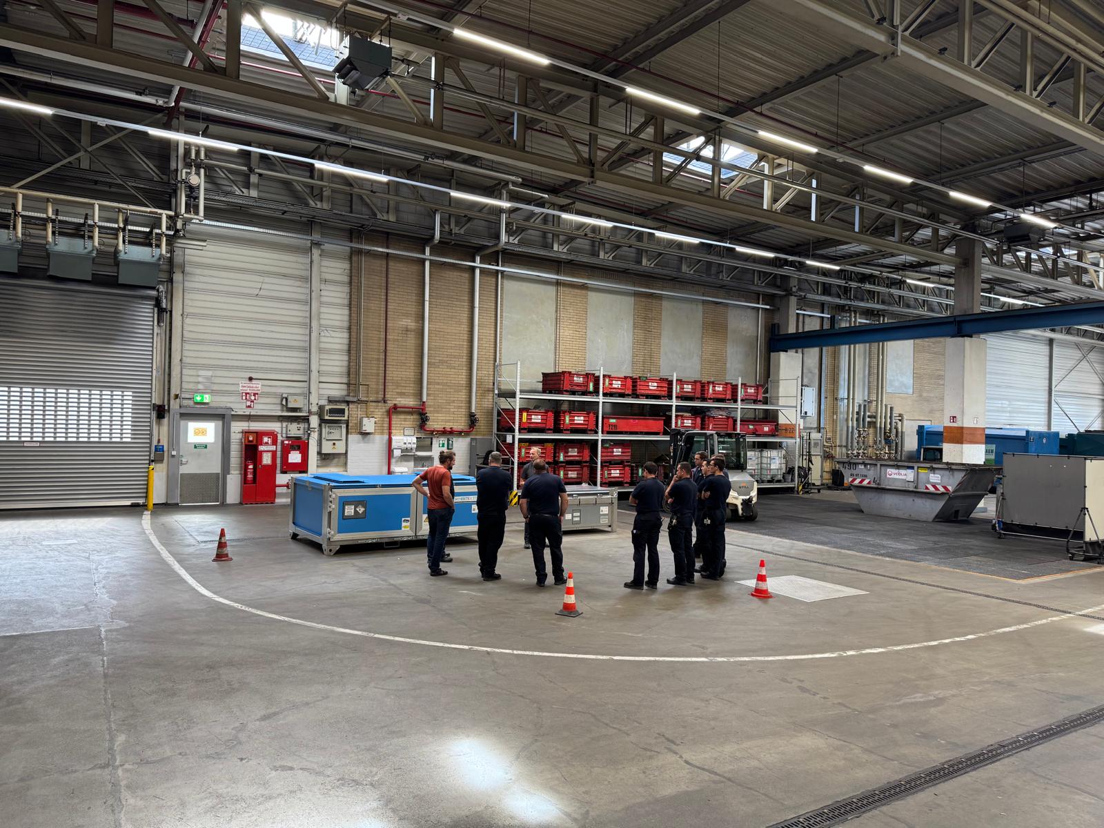 Mehrere Personen stehen in einer großen Halle, umgeben von Industriemaschinen.