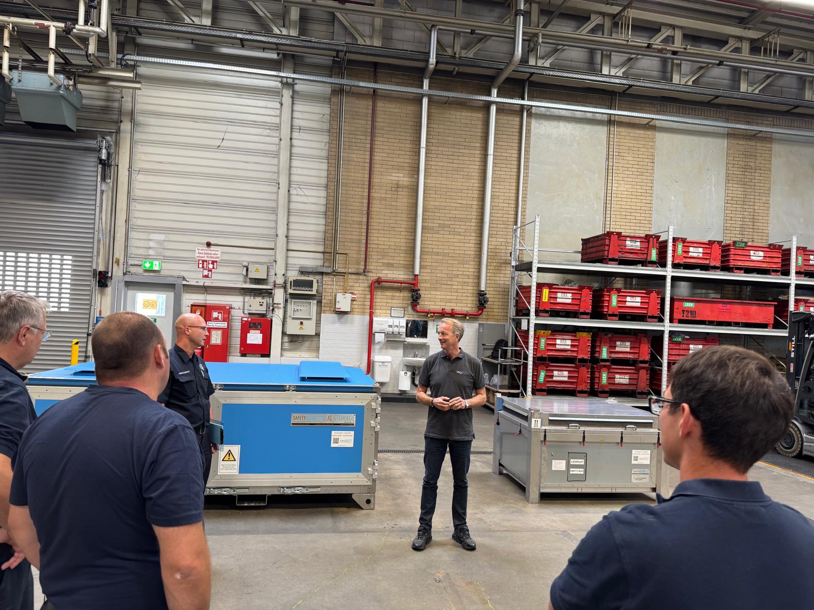 Eine Person spricht zu einer Gruppe in einer Industriehalle.