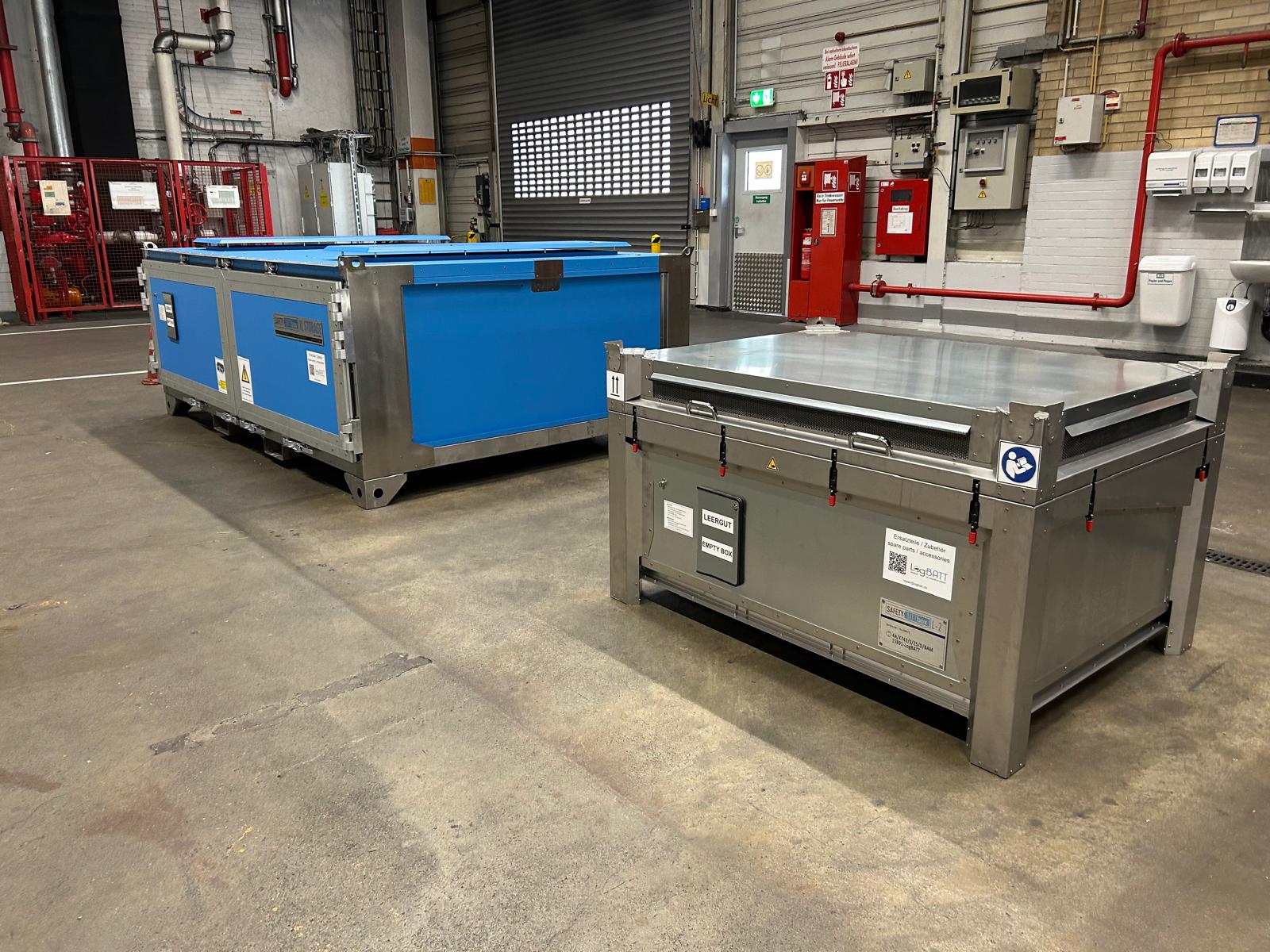 Ein blauer und ein grauer Cargo-Container stehen in einer Lagerhalle.