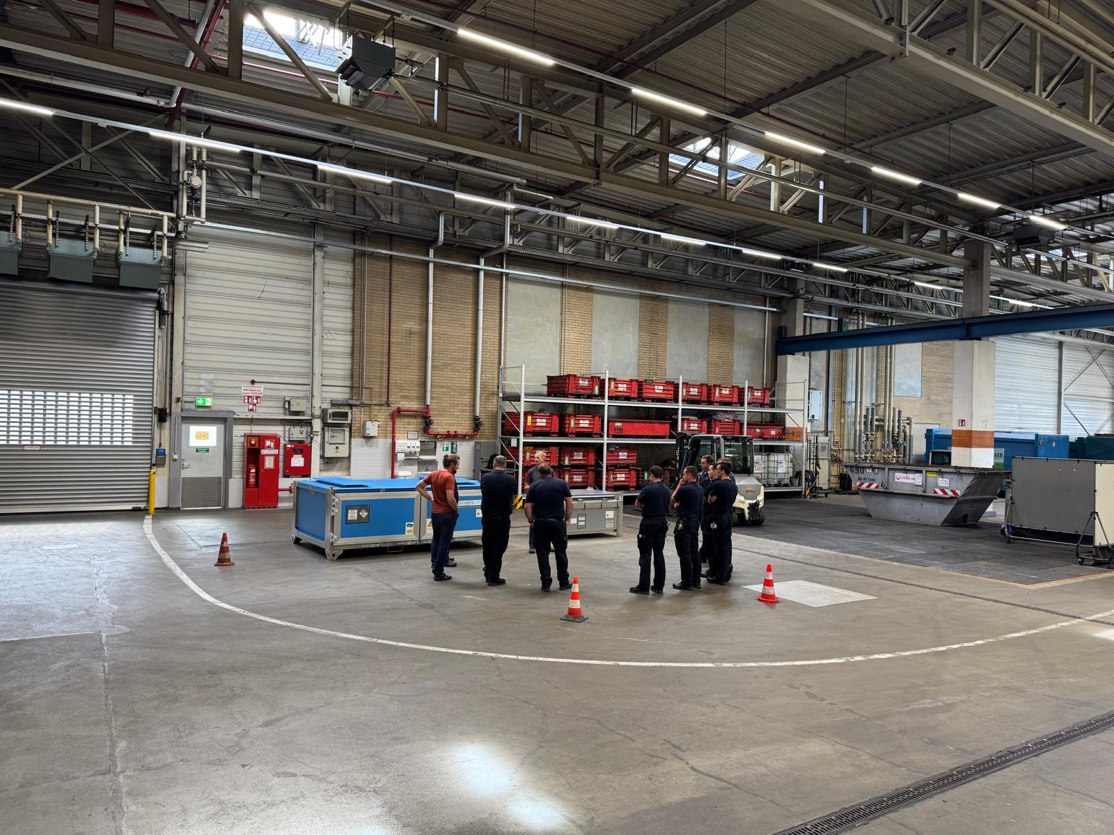 Mehrere Personen stehen in einer großen, gut beleuchteten Industrielagerhalle.
