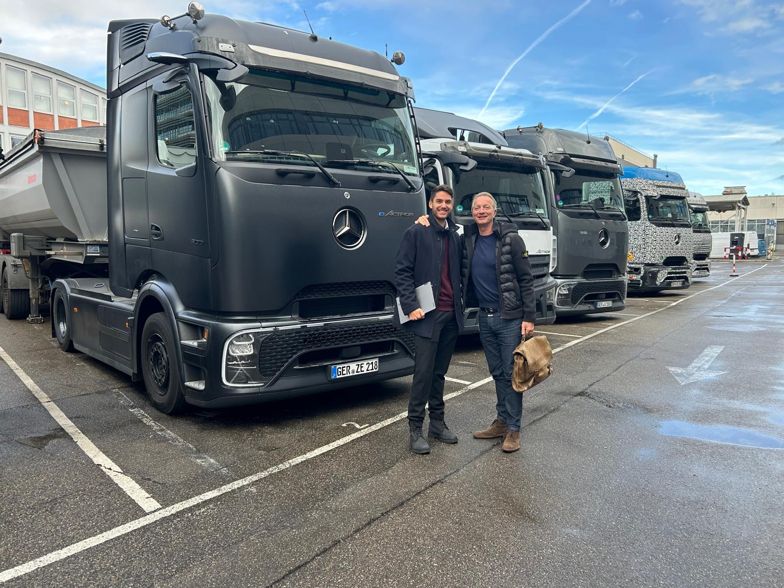 Zwei lächelnde Männer stehen vor schwarzen Mercedes Lastwagen auf einem Parkplatz